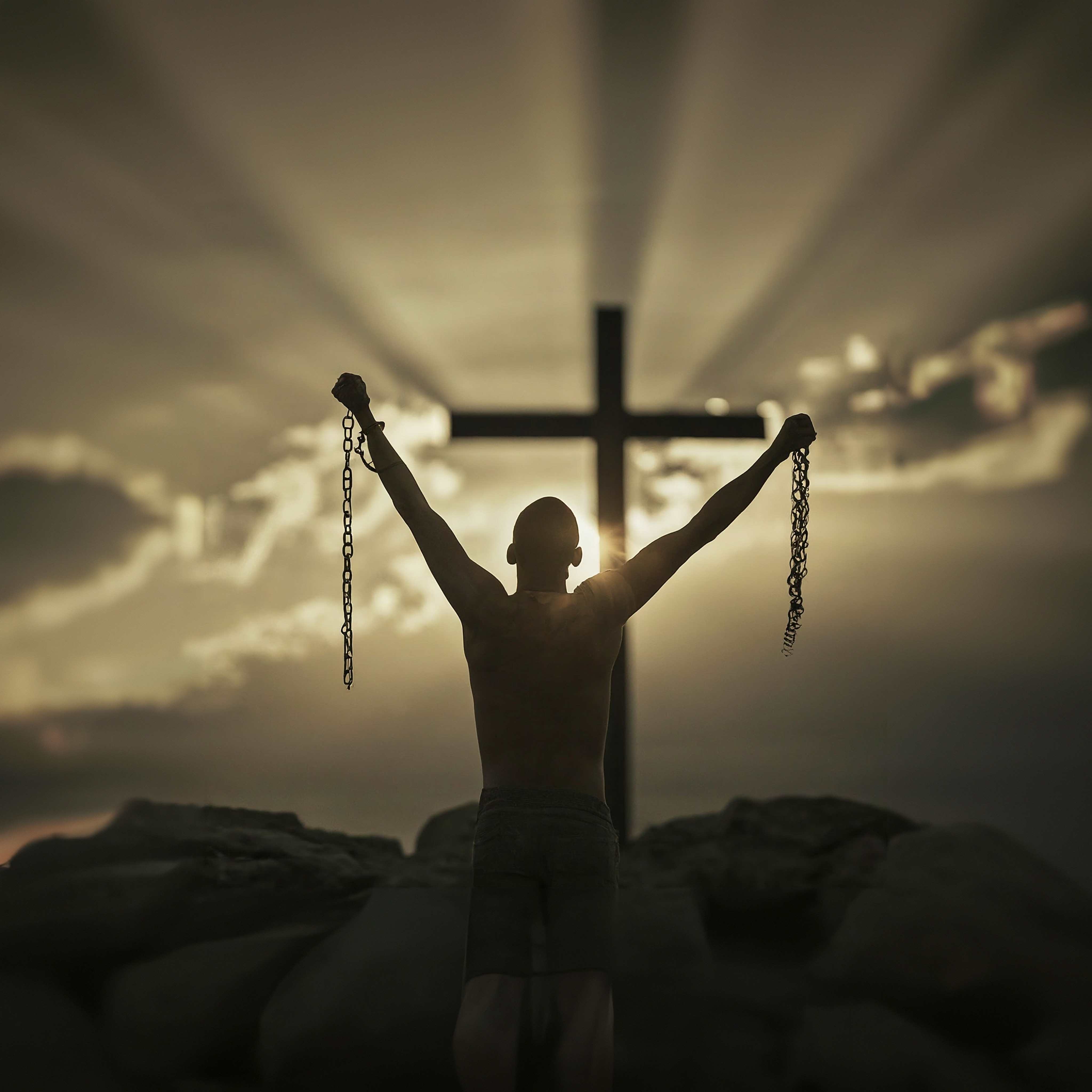 Photo of a man in front of a cross with his chains broken.